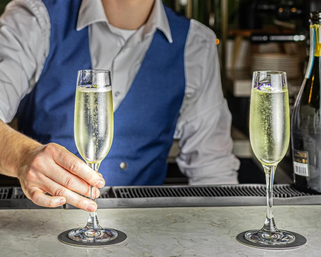 A person holding two champagne glasses on a bar at Lansdown Grove Hotel in Bath